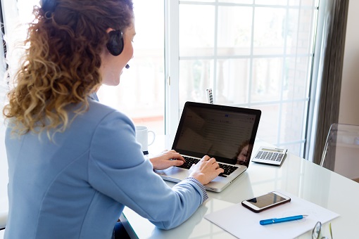 Na imagem uma mulher em frente a um computador realizando o trabalho de Call Center